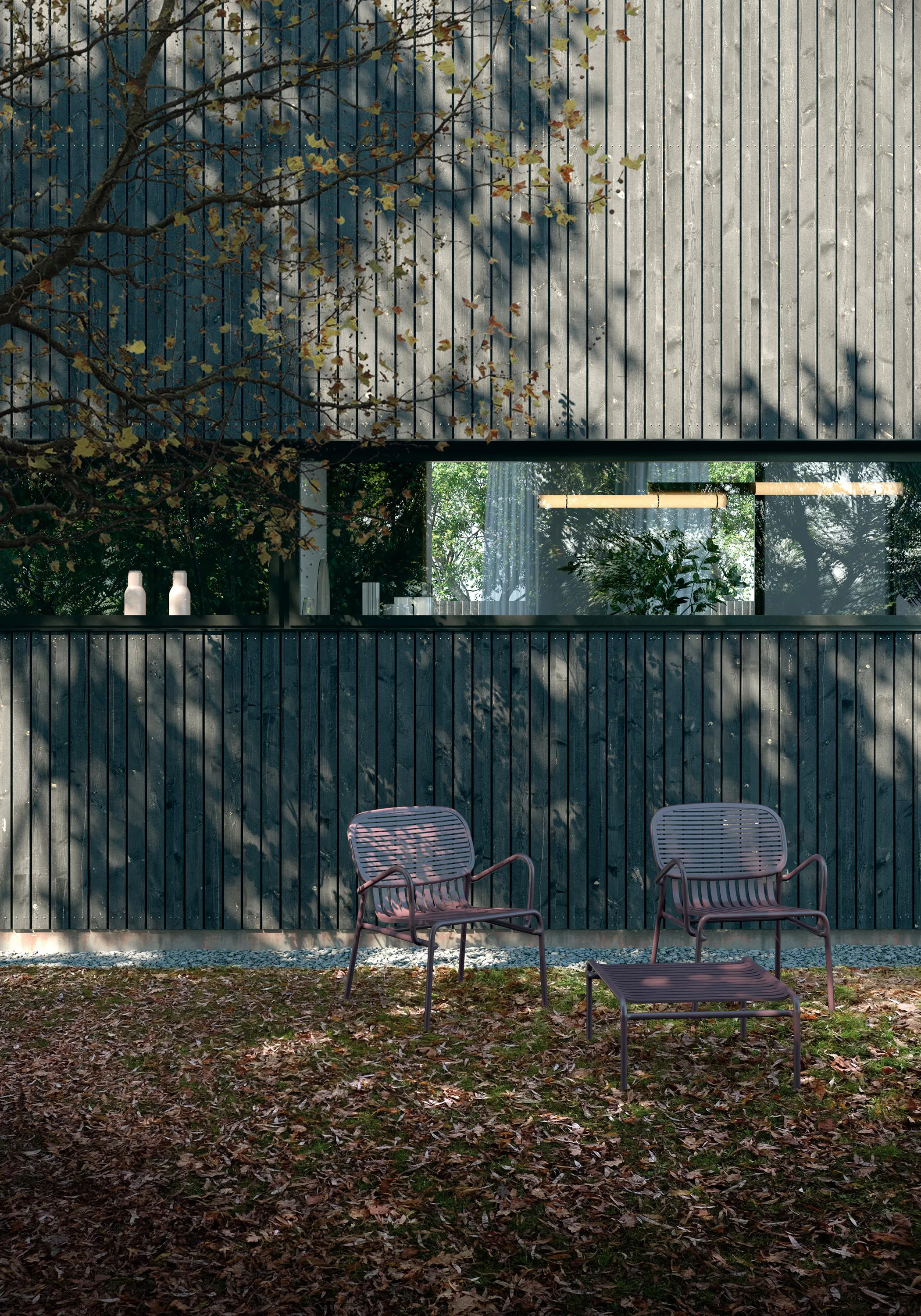 Dark timber-clad facade of a Green Harbor house with a long window and two chairs on fallen autumn leaves.